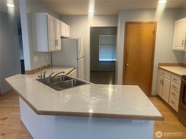 kitchen featuring a sink, a peninsula, tile countertops, and light wood finished floors