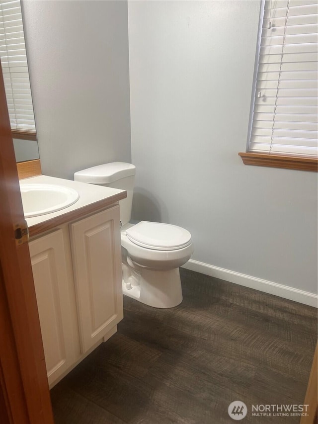 half bath featuring baseboards, toilet, wood finished floors, and vanity