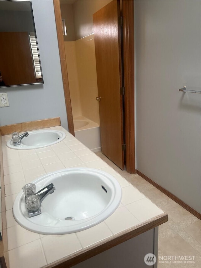 bathroom featuring double vanity, bathing tub / shower combination, baseboards, and a sink