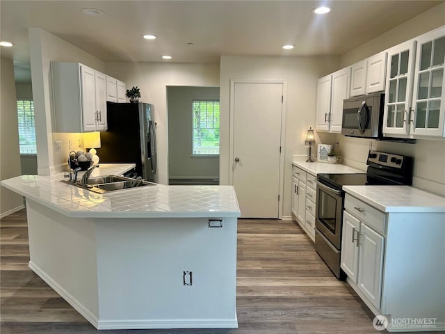 kitchen featuring a peninsula, dark wood-type flooring, tile countertops, a sink, and appliances with stainless steel finishes