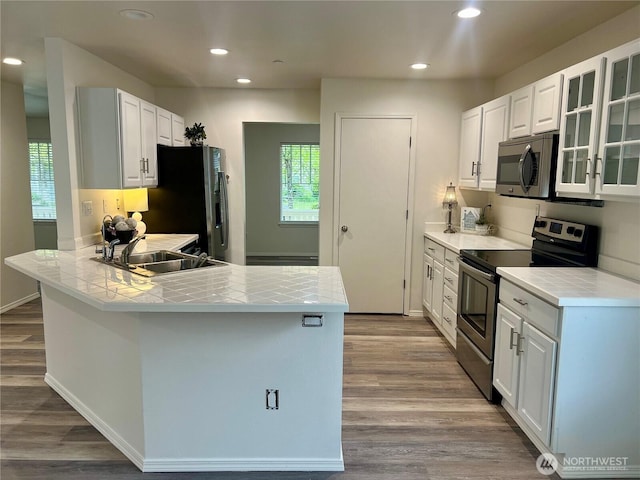 kitchen featuring dark wood-style flooring, a peninsula, a sink, a wealth of natural light, and stainless steel appliances