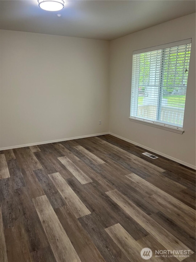 spare room with visible vents, baseboards, and dark wood-style floors