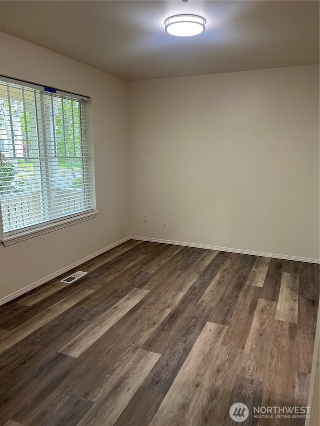 unfurnished room with baseboards, dark wood finished floors, and visible vents