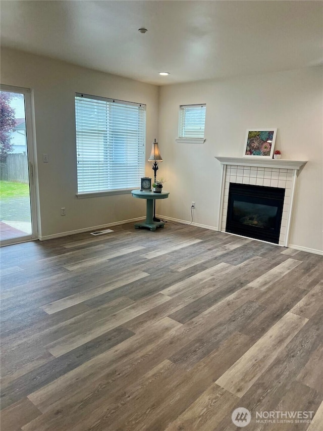 unfurnished living room with baseboards, a tiled fireplace, wood finished floors, and a healthy amount of sunlight