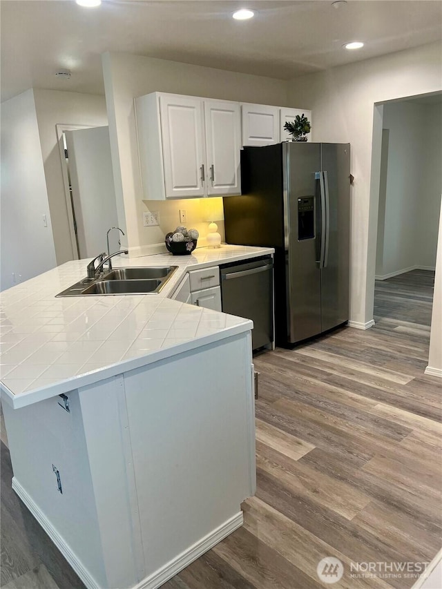 kitchen featuring appliances with stainless steel finishes, wood finished floors, a sink, a peninsula, and tile counters