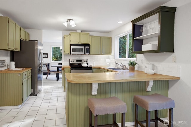 kitchen with a sink, appliances with stainless steel finishes, a peninsula, light tile patterned floors, and decorative backsplash