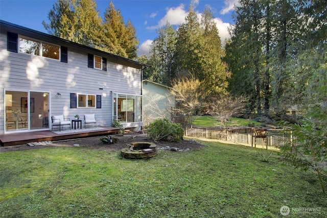 rear view of house with a yard, a fire pit, a deck, and fence