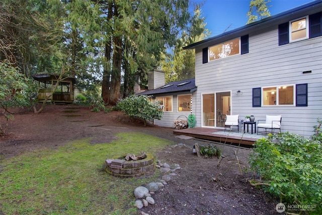 back of property with a wooden deck, a chimney, and an outdoor fire pit