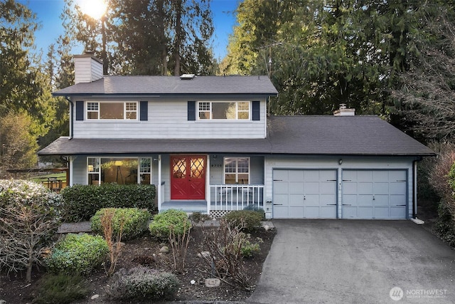 traditional-style home featuring a garage, driveway, covered porch, and a chimney