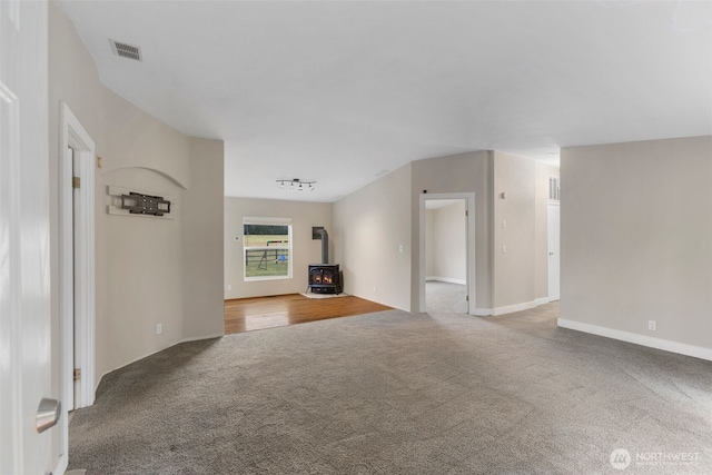 unfurnished living room featuring a wood stove, carpet, and visible vents