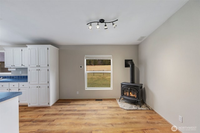 unfurnished living room featuring a wood stove, light wood-style floors, and visible vents