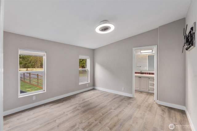 unfurnished bedroom with a sink, baseboards, light wood finished floors, and connected bathroom