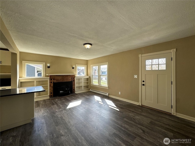 unfurnished living room with a baseboard radiator, a brick fireplace, dark wood finished floors, and baseboards