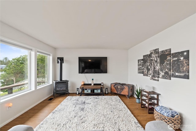 living room with visible vents, baseboards, wood finished floors, and a wood stove