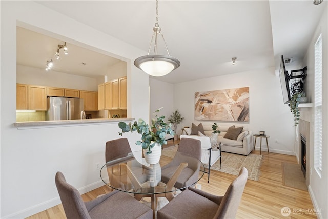 dining area featuring light wood-style flooring, a fireplace with flush hearth, and baseboards