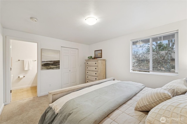 bedroom with ensuite bath, baseboards, a closet, and light carpet