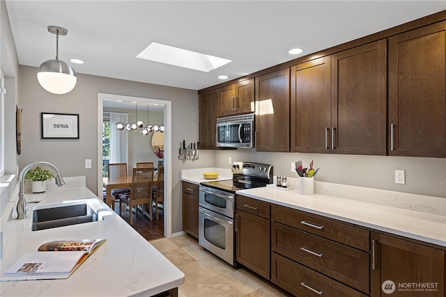 kitchen featuring light stone countertops, a sink, dark brown cabinetry, appliances with stainless steel finishes, and pendant lighting