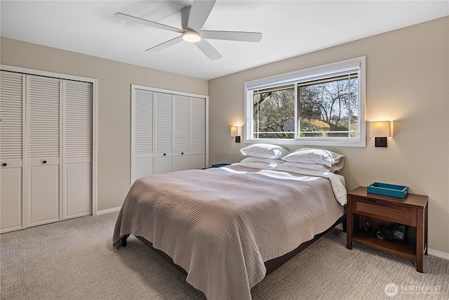 bedroom featuring light carpet, ceiling fan, baseboards, and multiple closets