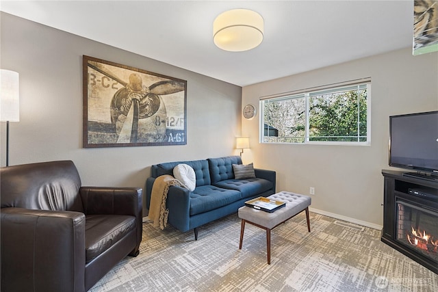 living area featuring a glass covered fireplace, visible vents, and baseboards