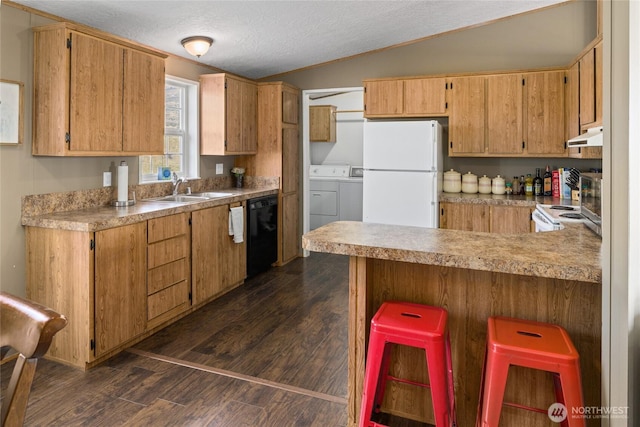 kitchen with white appliances, dark wood finished floors, a sink, under cabinet range hood, and washing machine and dryer