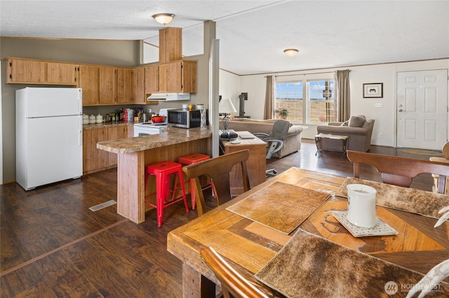 kitchen featuring white appliances, dark wood-style floors, a peninsula, extractor fan, and vaulted ceiling