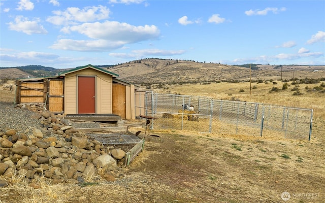 view of outdoor structure with a rural view, an outbuilding, fence, and a mountain view