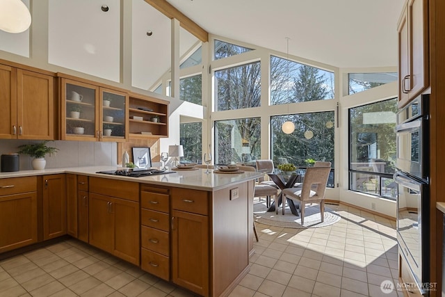 kitchen featuring glass insert cabinets, light countertops, light tile patterned floors, brown cabinetry, and stainless steel double oven