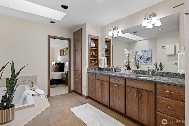 ensuite bathroom featuring double vanity, a skylight, a sink, a bath, and connected bathroom