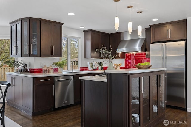 kitchen with dark wood-style flooring, stainless steel appliances, dark brown cabinets, wall chimney exhaust hood, and a center island