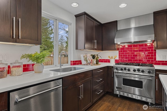 kitchen featuring light countertops, wall chimney exhaust hood, appliances with stainless steel finishes, and a sink