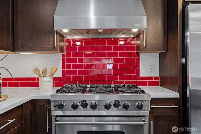 kitchen featuring dark brown cabinets, tasteful backsplash, appliances with stainless steel finishes, and wall chimney range hood