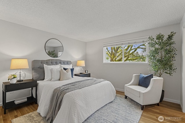 bedroom with a textured ceiling, baseboards, and wood finished floors