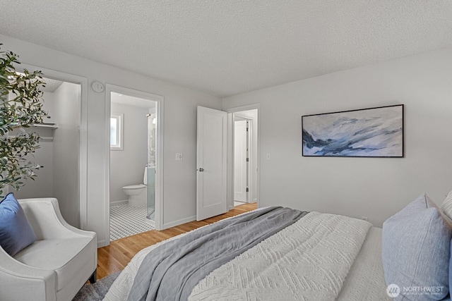 bedroom with baseboards, a textured ceiling, ensuite bath, and light wood-style floors