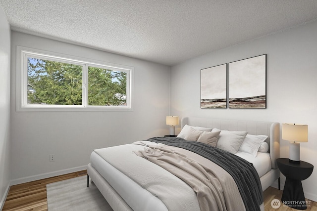 bedroom with a textured ceiling, baseboards, and wood finished floors