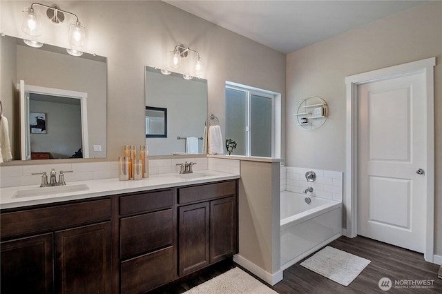 full bathroom with double vanity, wood finished floors, a sink, and a bath