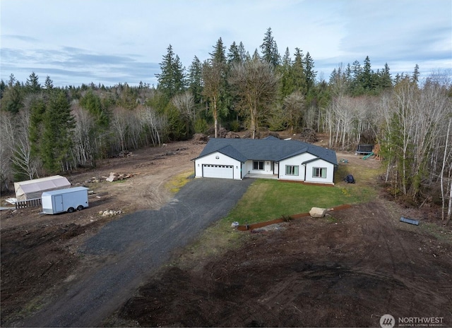 view of front of house featuring a garage, dirt driveway, a front lawn, and a view of trees