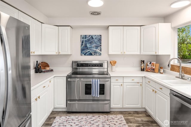 kitchen with wood finished floors, a sink, stainless steel appliances, light countertops, and white cabinetry