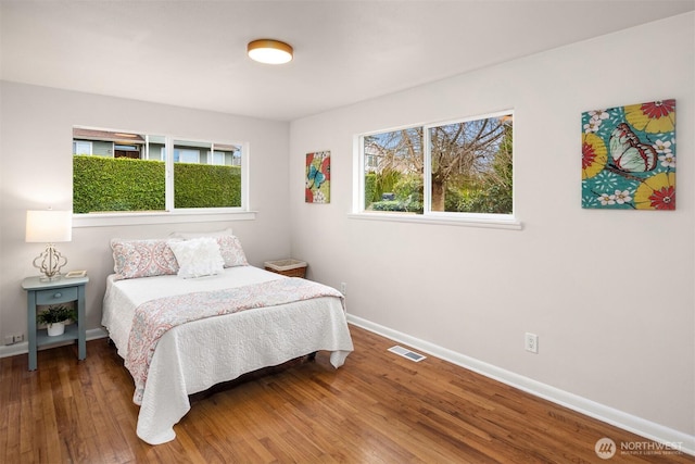 bedroom with visible vents, multiple windows, baseboards, and wood finished floors