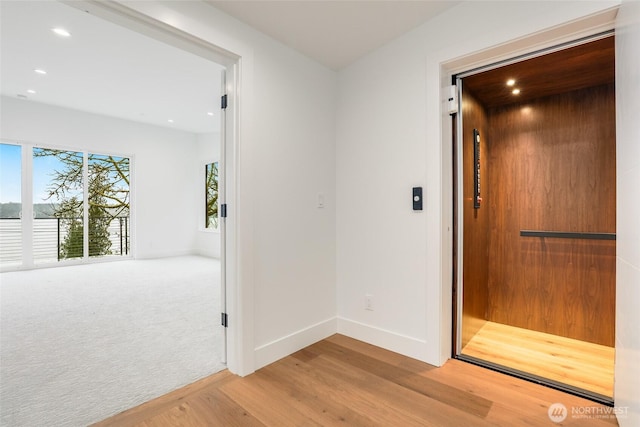 hallway with baseboards, carpet floors, elevator, recessed lighting, and wood finished floors