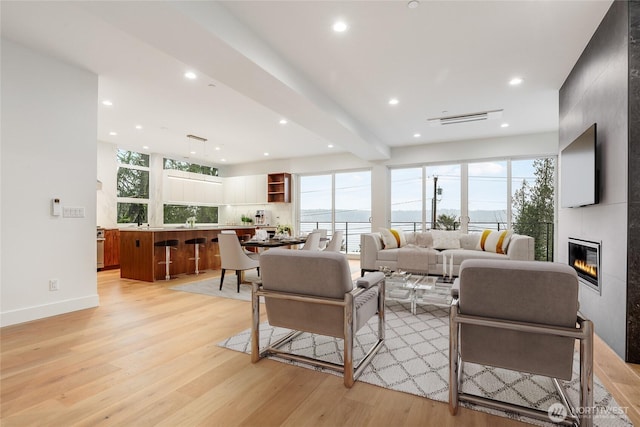 living area featuring beam ceiling, recessed lighting, a fireplace, and light wood-type flooring