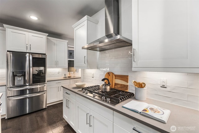 kitchen featuring dark wood-type flooring, appliances with stainless steel finishes, wall chimney exhaust hood, and white cabinetry