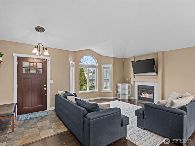 living room with baseboards, an inviting chandelier, lofted ceiling, a fireplace with flush hearth, and dark wood-type flooring