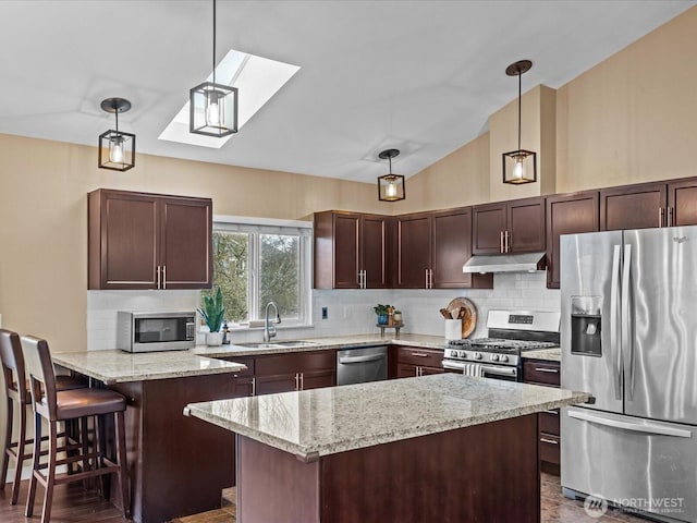 kitchen with light stone countertops, a sink, under cabinet range hood, appliances with stainless steel finishes, and tasteful backsplash