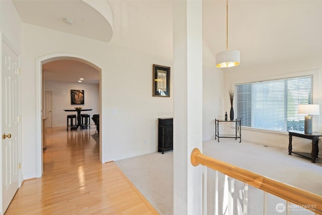 hallway with baseboards, light colored carpet, light wood-style flooring, a towering ceiling, and arched walkways