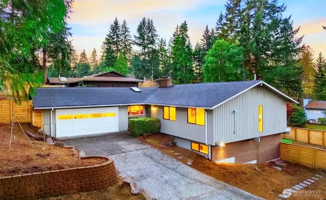 view of front facade featuring fence, a shingled roof, a chimney, a garage, and aphalt driveway