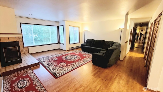 living room with baseboard heating, wood finished floors, and a tile fireplace