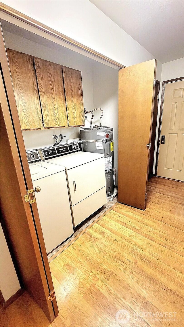 clothes washing area with cabinet space, electric water heater, light wood-style flooring, and washer and clothes dryer