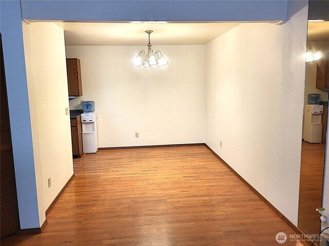 unfurnished dining area with light wood-style flooring, an inviting chandelier, and baseboards