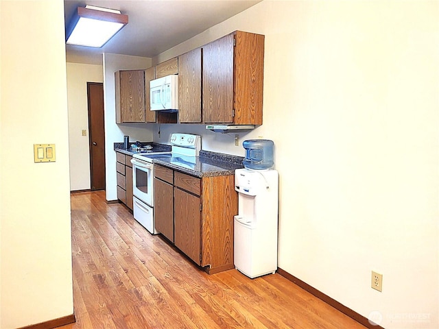 kitchen with light wood-type flooring, dark countertops, white appliances, and baseboards