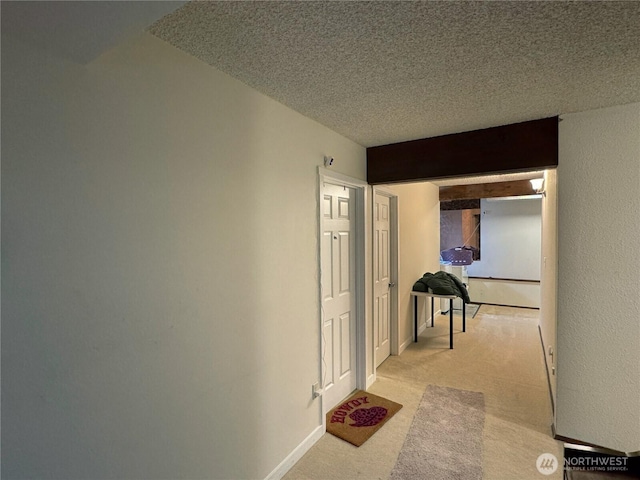 hall featuring light colored carpet, a textured ceiling, and baseboards